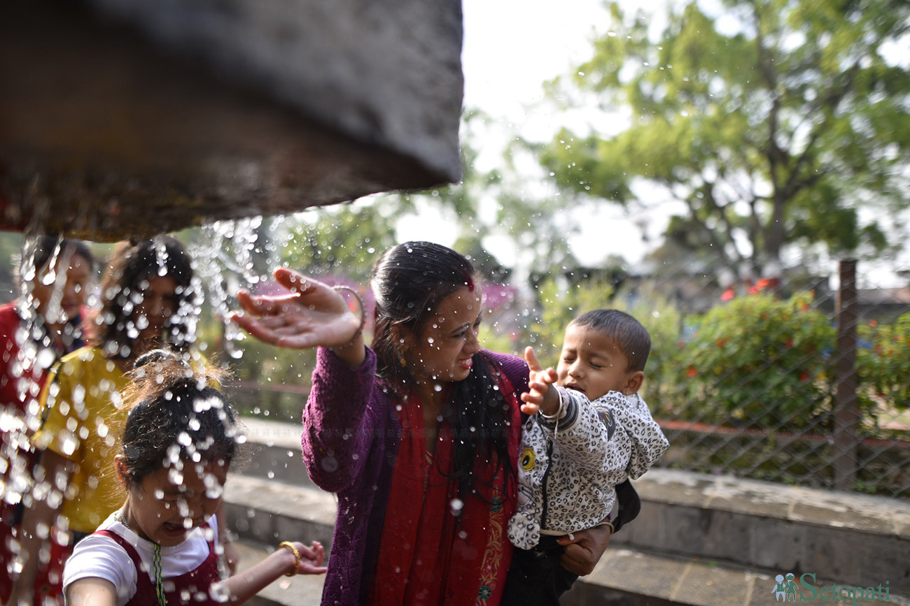 बालाजु मेलामा बच्चा लिएर आएको एक श्रद्धालु बाइसधारामा बच्चालाई स्नान गराउँदै। तस्बिरः नारायण महर्जन